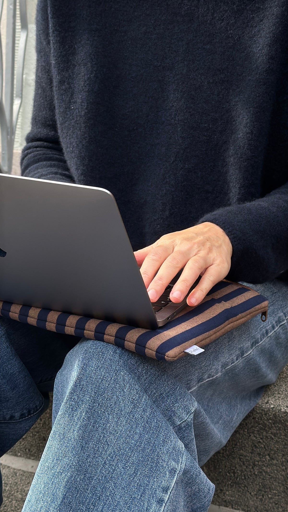 Gepolsterte Laptoptasche navy/braun gestreift auf dem Schoß, darauf ein Laptop